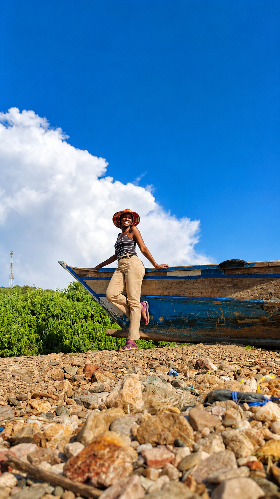 Eva smiling beside a blue wooden boat on the shore